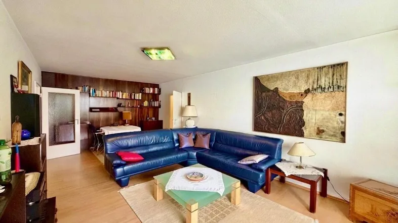 Geräumiges Wohnzimmer mit blauer Ledercouch, Holzboden und Bücherregal.