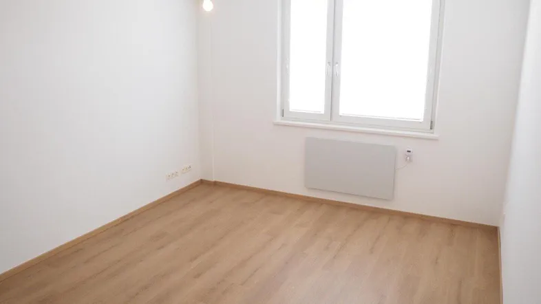 Helles, leeres Zimmer mit Laminatboden und großem Fenster, ideal als Schlafzimmer oder Büro.