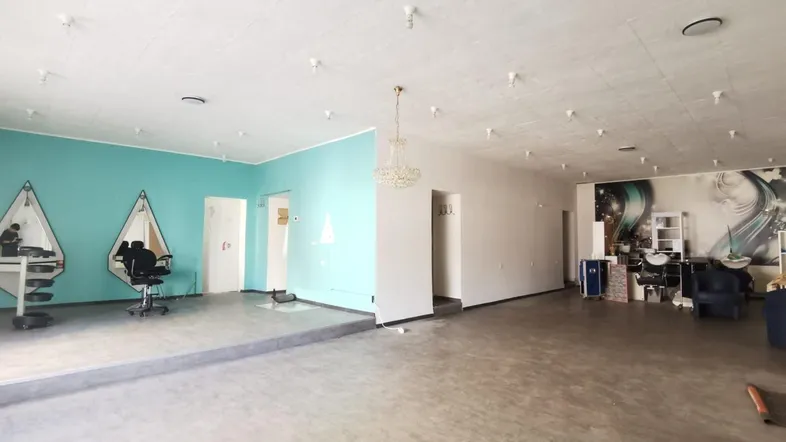 Großer offener Gewerberaum mit erhöhter Fläche, türkiser Wandakzent und Kronleuchter, ideal für ein Studio.