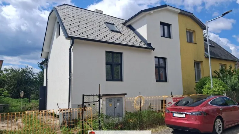Außenansicht des Hauses mit frisch gestrichener Fassade und angrenzendem älteren Gebäudeteil.