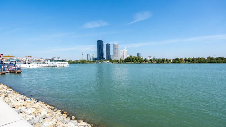 Weitläufiger Blick über ein Gewässer auf die moderne Skyline einer Stadt mit Hochhäusern.