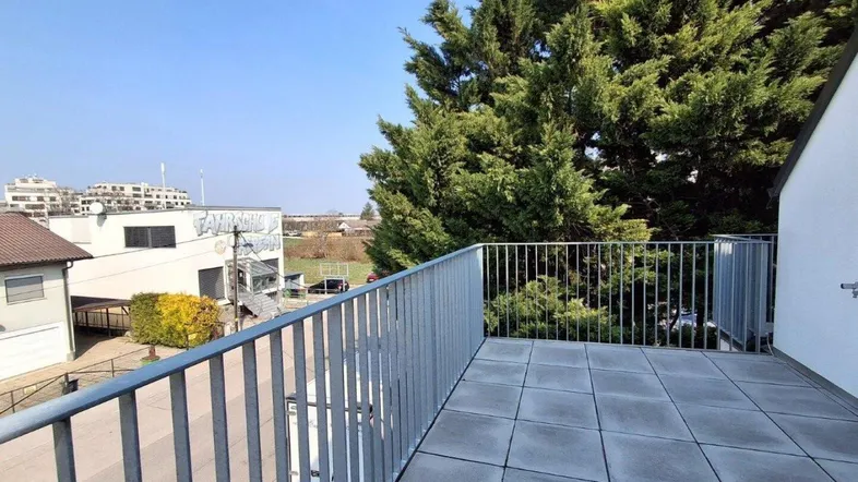 Geräumiger Balkon mit Fliesenboden und Blick ins Grüne, umgeben von hohen Bäumen.
