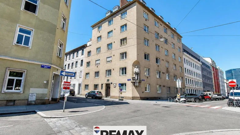 Gebäude an einer Straßenecke mit mehreren Etagen und Fenstern in urbaner Umgebung.
