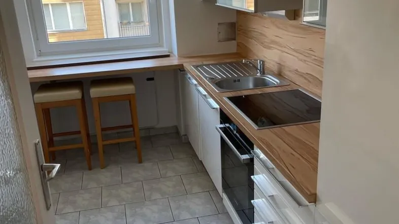 Moderne Küche mit weißen Schränken, Holzarbeitsplatte, integrierten Geräten und einem kleinen Essbereich am Fenster.