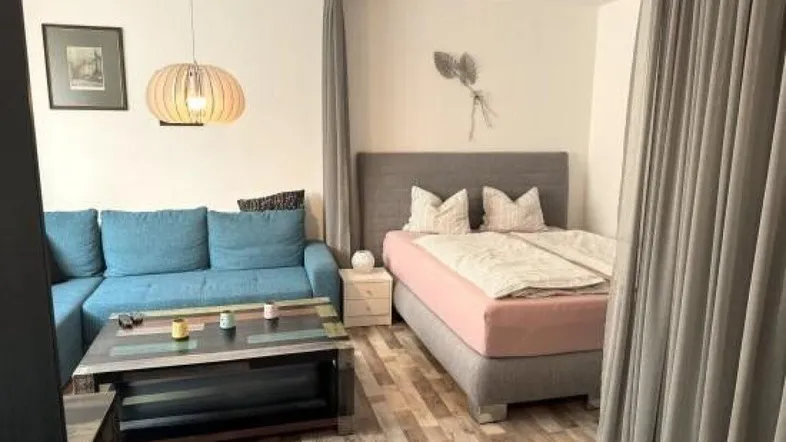 Gemütlicher Wohnbereich mit Sofa, Couchtisch und abgetrenntem Schlafbereich durch Vorhänge.