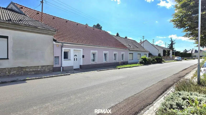 Ansicht der Immobilie von der Straße aus, mit angrenzenden Häusern und blauem Himmel.