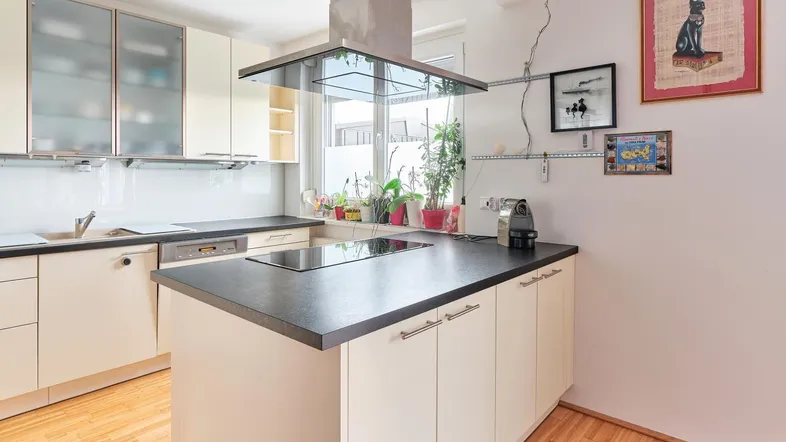 Moderne Küche mit Kochinsel, Induktionskochfeld und hellen Schränken, gut beleuchtet durch ein Fenster.