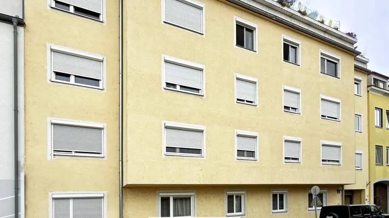 Gelbe Fassade eines Mehrfamilienhauses mit vielen Fenstern und Rollläden.