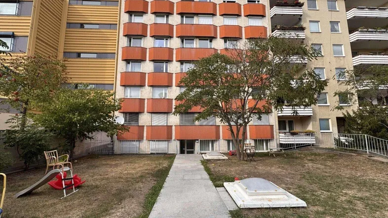 Mehrfamilienhaus mit orangefarbener Fassade und Grünfläche im Vordergrund.
