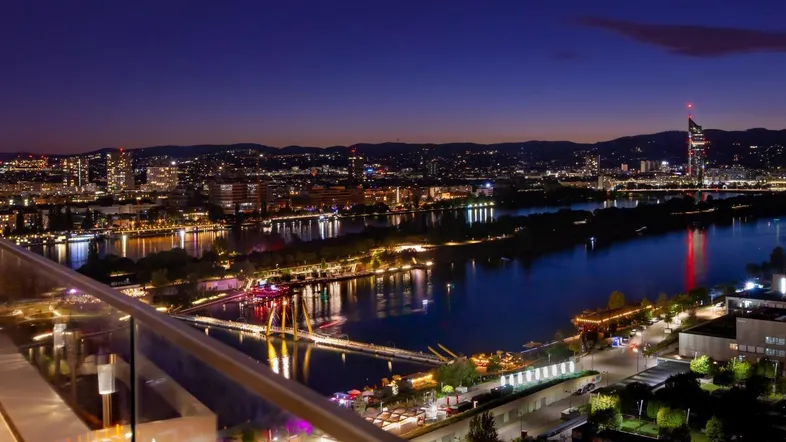 Nächtlicher Panoramablick auf die beleuchtete Stadt und den Fluss von einem Balkon.