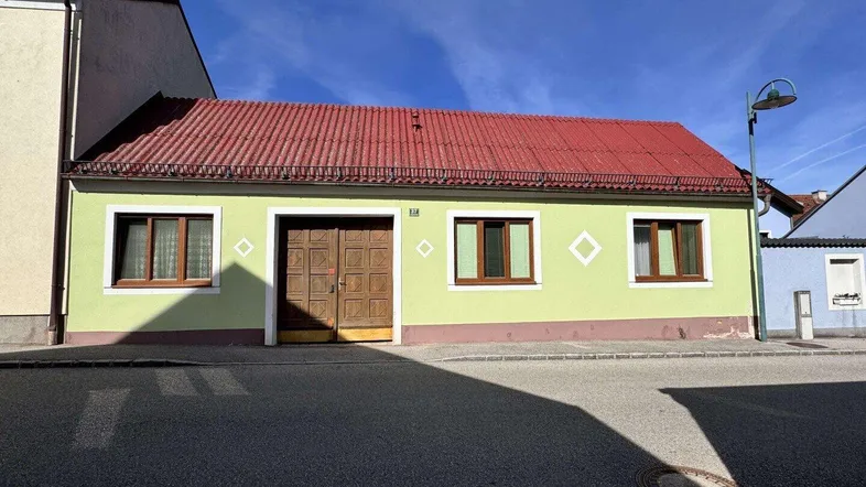 Traditionelles Haus mit hellgrüner Fassade und rotem Ziegeldach an einer ruhigen Straße.