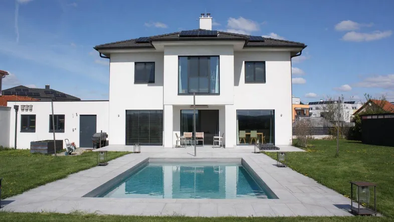 Modernes Einfamilienhaus mit weißer Fassade, Garten und privatem Swimmingpool unter blauem Himmel.