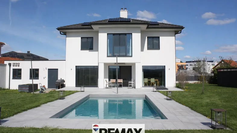 Modernes Einfamilienhaus mit privatem Pool und gepflegtem Garten unter blauem Himmel.