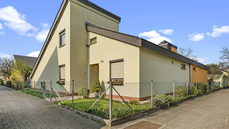 Modernes Einfamilienhaus mit heller Fassade, schrägem Dach und kleinem Vorgarten.