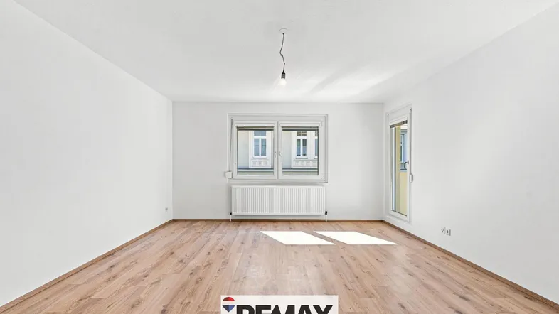 Helles, leeres Zimmer mit Laminatboden und Zugang zu einem Balkon oder einer Loggia.