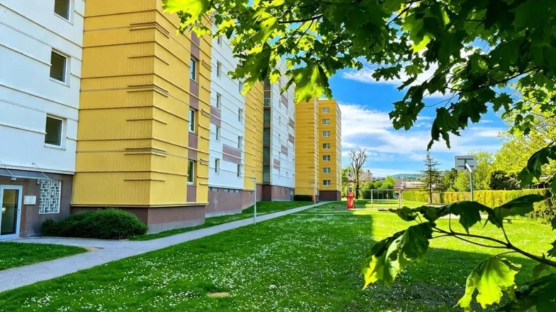 Mehrere Wohngebäude mit gelber Fassade und grüner Rasenfläche unter blauem Himmel.