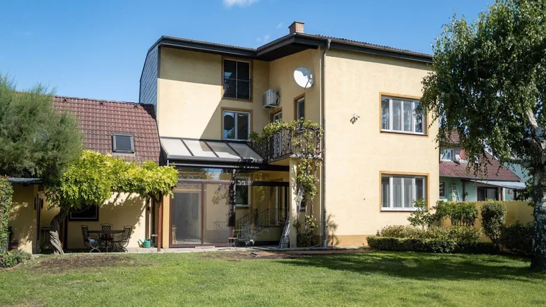 Rückansicht des Hauses mit großem Garten, Rasenfläche und überdachtem Sitzbereich im Freien.