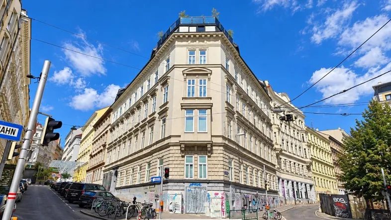 Historisches Eckgebäude mit klassischer Fassade und Blick auf die belebte Stadtstraße unter blauem Himmel.