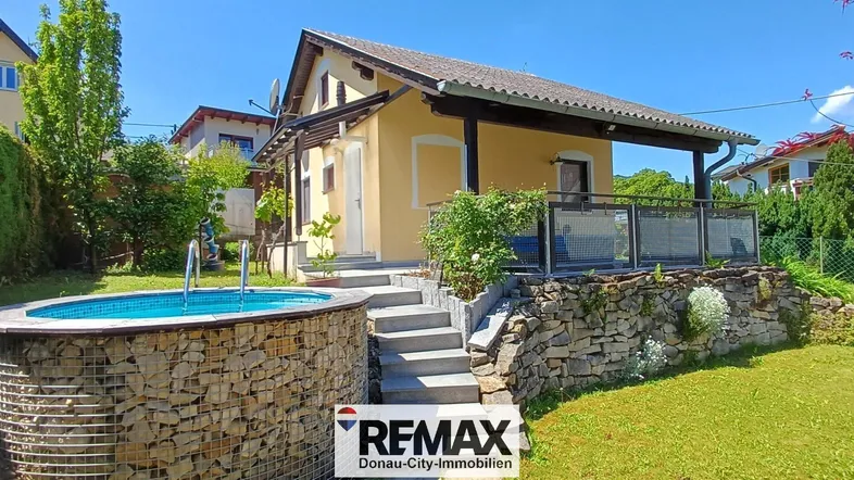 Gelbes Haus mit Pool im Garten, umgeben von Grünflächen und einer Steinmauer.