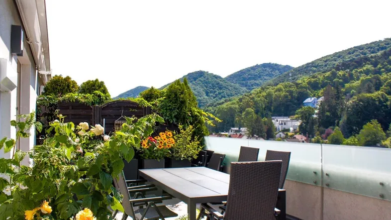 Große Sonnenterrasse mit Gartenmöbeln, Pflanzen und einem weiten Blick auf grüne Hügel.