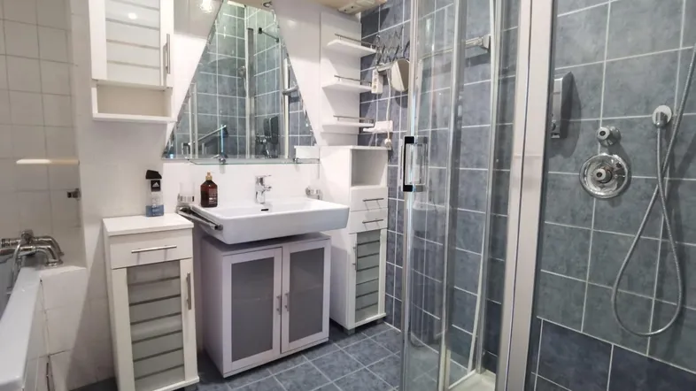 Funktionales Badezimmer mit blauen Fliesen, Duschkabine und integriertem Waschtisch.