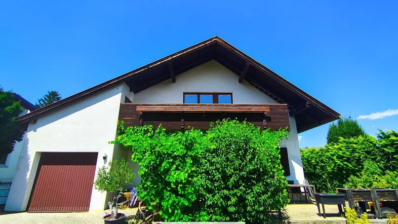 Vorderansicht des Hauses mit Garage, begrüntem Vorgarten und Balkon im Obergeschoss.