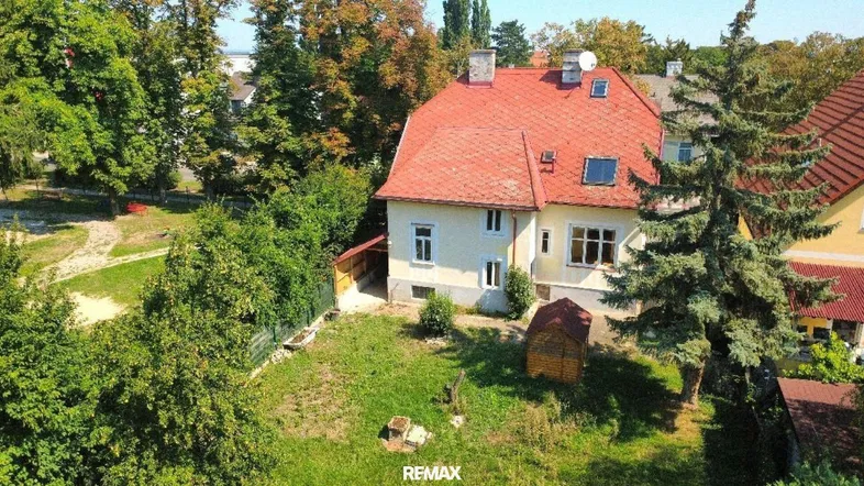 Luftaufnahme eines Hauses mit rotem Ziegeldach und großem Garten, umgeben von Bäumen.