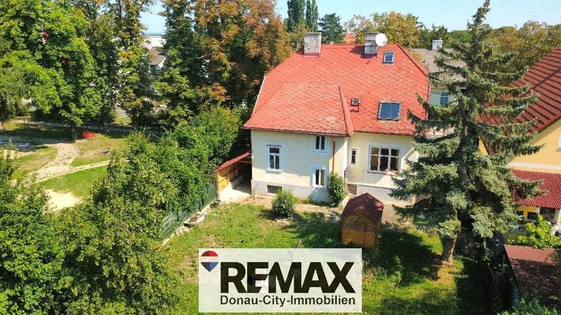 Luftaufnahme des Hauses mit rotem Ziegeldach und großem Gartenbereich umgeben von Bäumen.