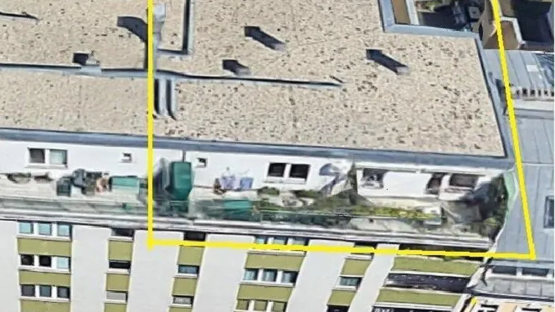 Luftaufnahme des Gebäudes mit hervorgehobener Dachterrasse und umliegenden Dächern der Stadt.