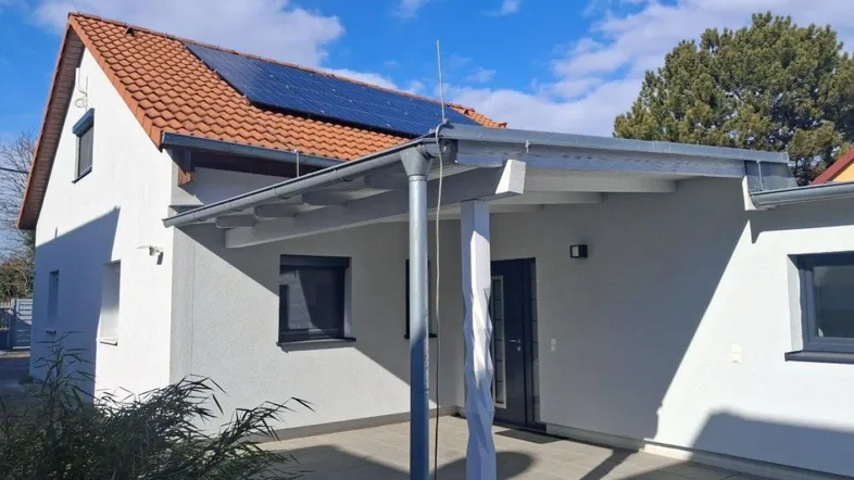 Modernes Einfamilienhaus mit überdachter Terrasse, Solaranlage auf dem Dach und gepflegtem Außenbereich.