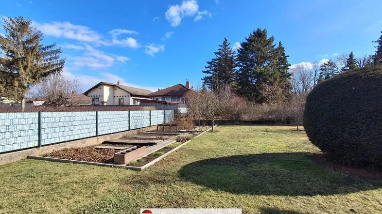 Großer Gartenbereich mit Rasenfläche und Hecke, umgeben von weiteren Wohnhäusern unter blauem Himmel.