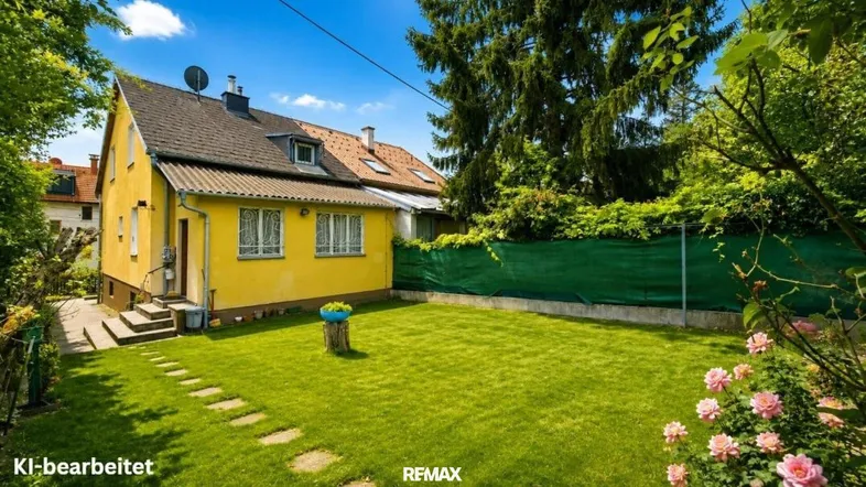 Gepflegter Gartenbereich mit Rasenfläche und einem gelben Einfamilienhaus im Hintergrund unter blauem Himmel.