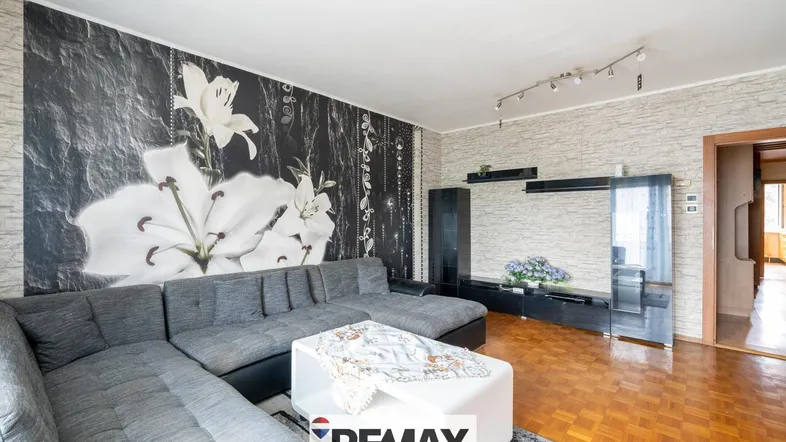 Geräumiges Wohnzimmer mit großem Ecksofa, floraler Tapete und Parkettboden, gut gepflegt.