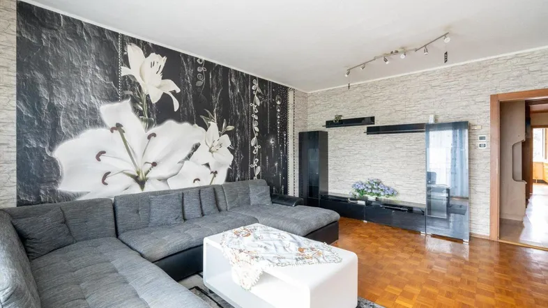 Helles Wohnzimmer mit großem Ecksofa, Parkettboden und auffälliger Blumentapete.