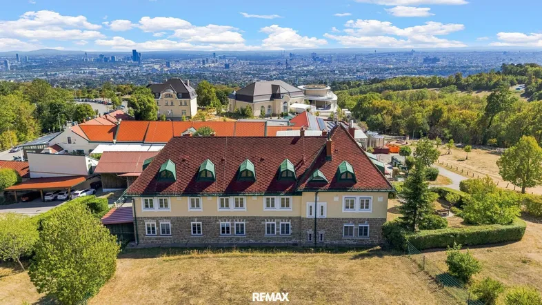 Luftaufnahme eines weitläufigen Anwesens mit mehreren Gebäuden und Blick auf die Stadt.