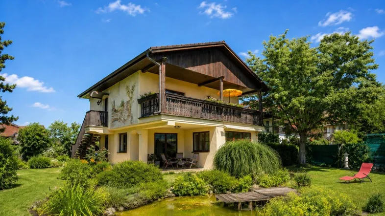 Charmantes Haus mit großem Garten, Teich und Balkon, umgeben von viel Grün.