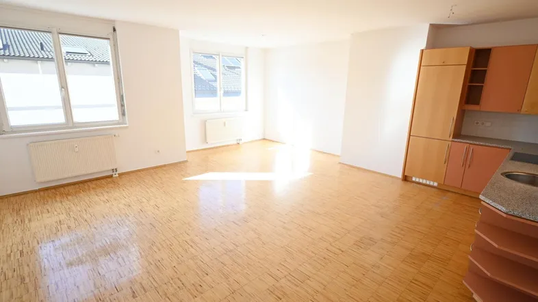Helles Wohnzimmer mit integrierter Küchenzeile, Holzfußboden und großen Fenstern, die viel Licht hereinlassen.