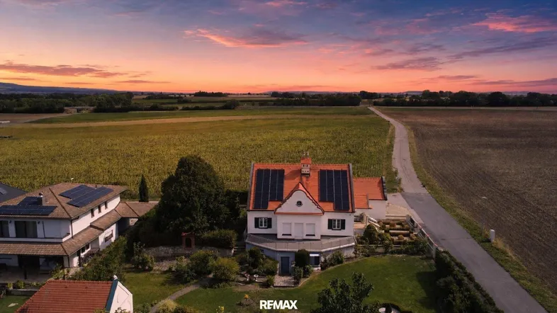 Luftaufnahme eines Hauses mit Solaranlage und weiten Feldern bei Sonnenuntergang.