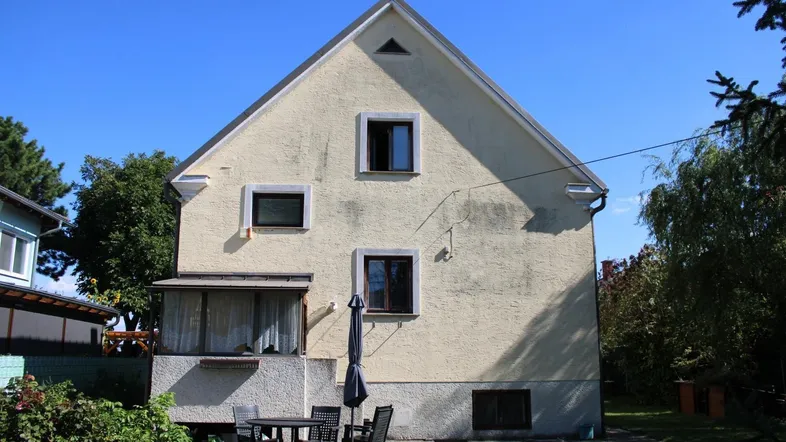 Rückansicht eines Einfamilienhauses mit Gartenbereich und kleiner Terrasse unter blauem Himmel.
