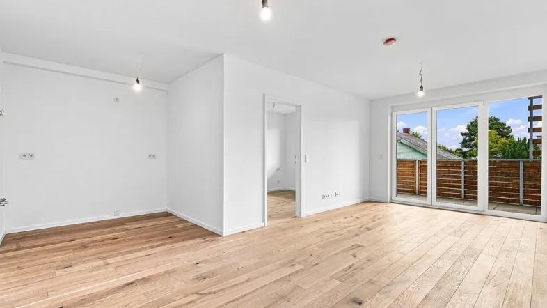 Helles, leeres Zimmer mit Holzboden und Zugang zu einem Balkon, ideal für Wohnzwecke.