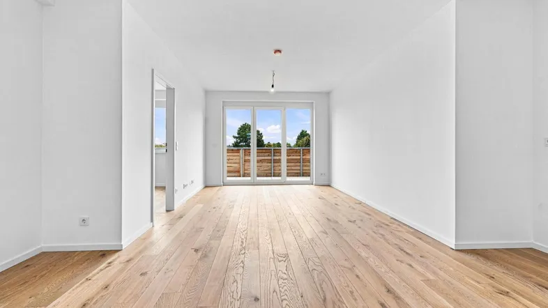 Helles, leeres Wohnzimmer mit Holzboden und Zugang zu einem Balkon, ideal für neue Einrichtungsideen.
