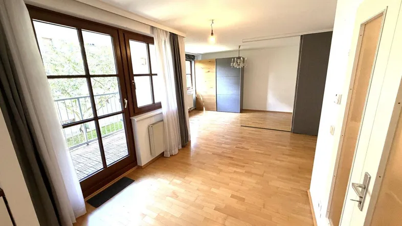 Helles Wohnzimmer mit Parkettboden und Zugang zu einem kleinen Balkon, bereit zur Einrichtung.