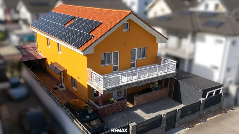 Luftaufnahme eines Einfamilienhauses mit leuchtend gelber Fassade, Balkon und Solaranlage auf dem Dach.