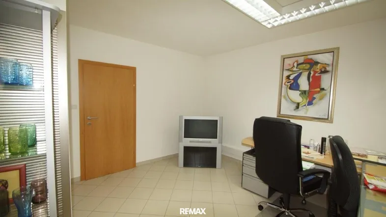 Helles Büro mit Fliesenboden, Schreibtisch und einem farbenfrohen Kunstwerk an der Wand.