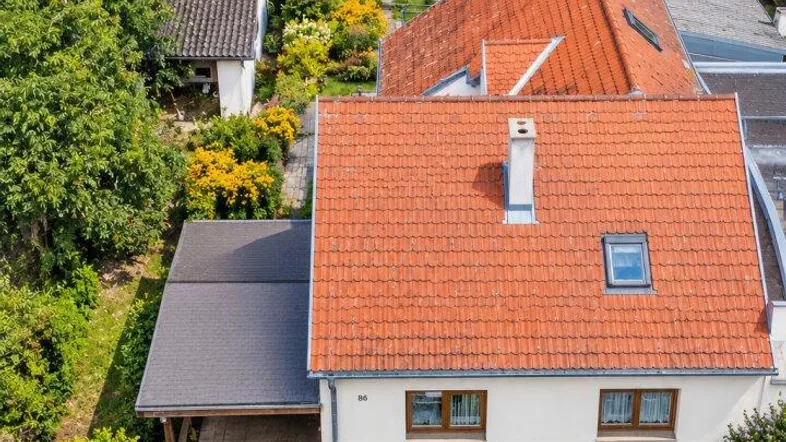 Luftaufnahme eines Einfamilienhauses mit rotem Ziegeldach, Carport und gepflegtem Vorgarten.
