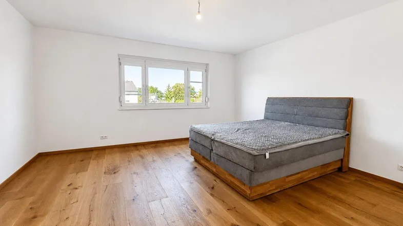 Helles Schlafzimmer mit Holzboden, weißen Wänden und einem großen Fenster für viel Tageslicht.