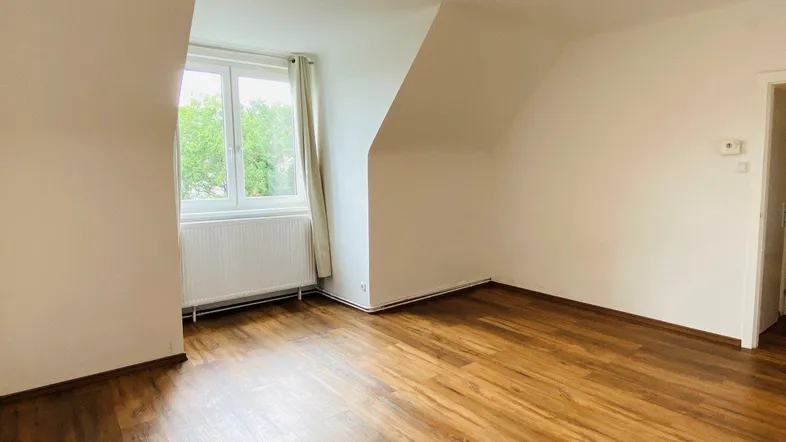 Helles Zimmer mit Dachschräge, Holzfußboden und Fenster mit Blick ins Grüne.