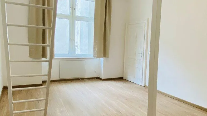 Helles Zimmer mit Hochbettkonstruktion, Holzfußboden und Fenster mit Vorhängen.