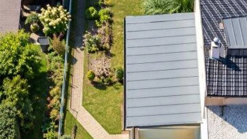 Luftaufnahme eines Einfamilienhauses mit langem Garten, Zufahrt und Carport.