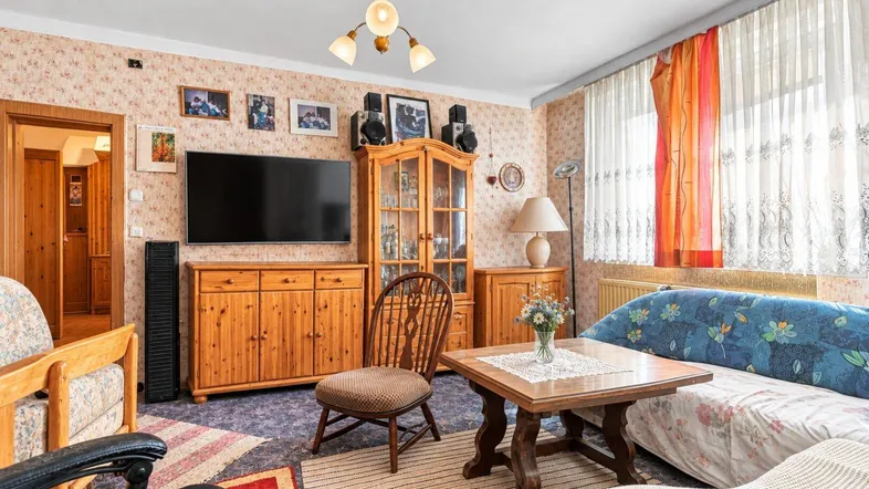 Gemütliches Wohnzimmer mit traditionellen Holzmöbeln, floraler Tapete und einem Fernseher.